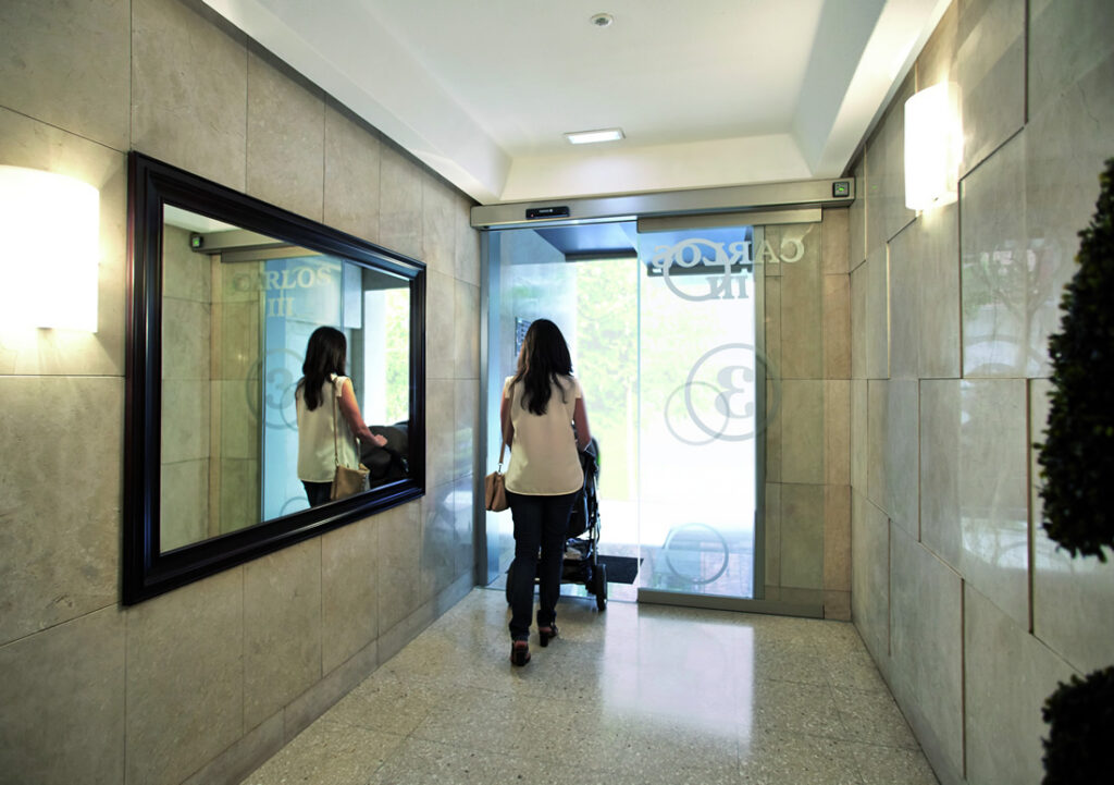 Madre accediendo con carrito de bebé a comunidad con puerta automática